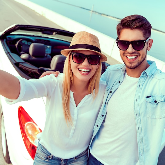 Capturing the bright moments. Top view of cheerful young couple making selfie while standing near their white convertible