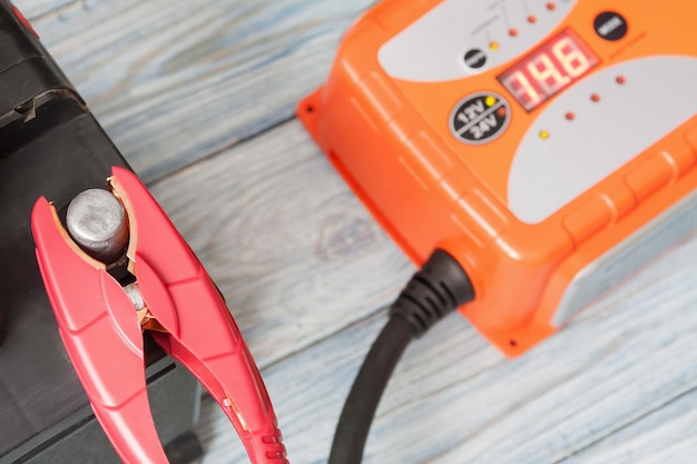 A car battery with red and black battery jumper clamps and a car battery charger