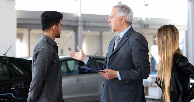 Car dealer exaplining a car's features to a couple by reading a document