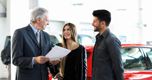 Car dealer reading a contract to a couple in an auto showroom