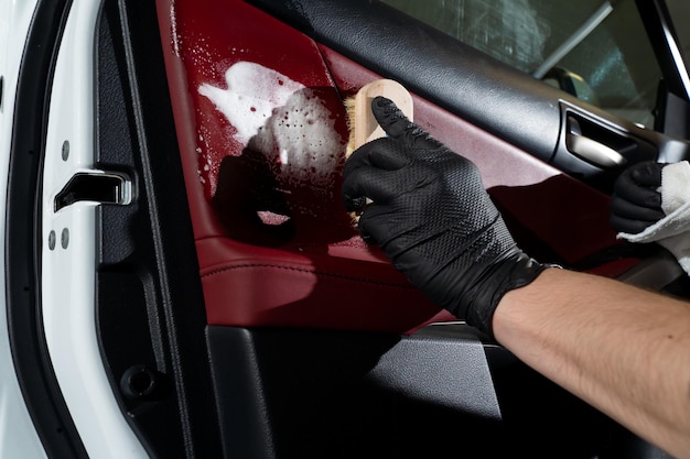 Car detailer cleans the auto door with brush and detergent Process of removing dust and dirt from the auto door panel