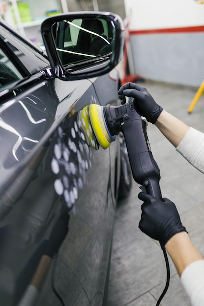 Car detailing - Worker with orbital polisher in auto repair shop. Selective focus.