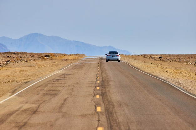 Car driving down road with visible mirage leading into desert mountains