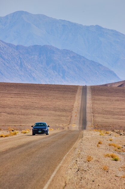 Car driving on long and bare road in empty desert landscape leading to mountains