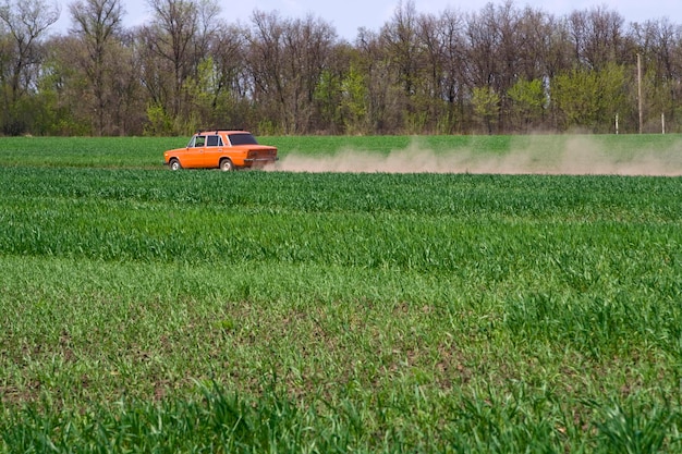 The car is driving along a country road with dust