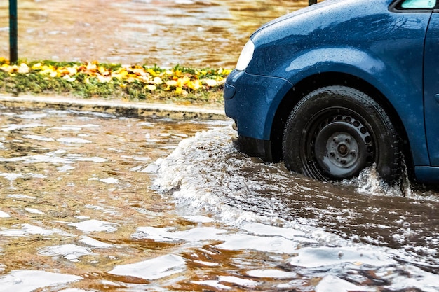 The car is driving through a puddle in heavy rain Splashes of water from under the wheels of a car Flooding and high water in the city