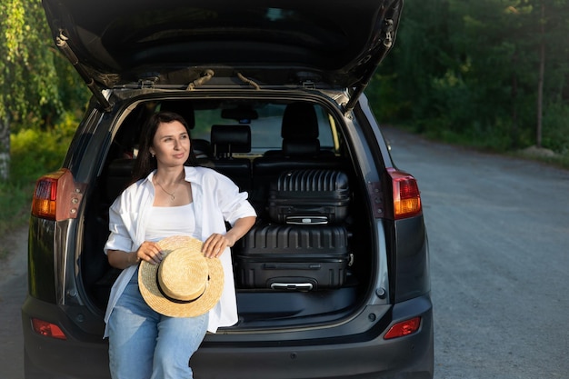 Car journey A young beautiful woman in a hat on vacation rests near the car Lifestyle