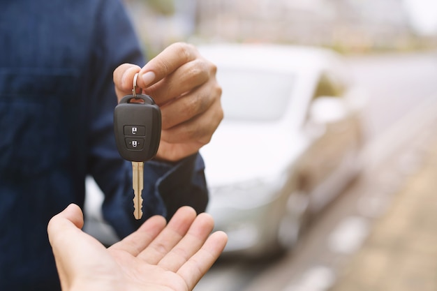 Car key, businessman handing over gives the car key to the other woman on car background.