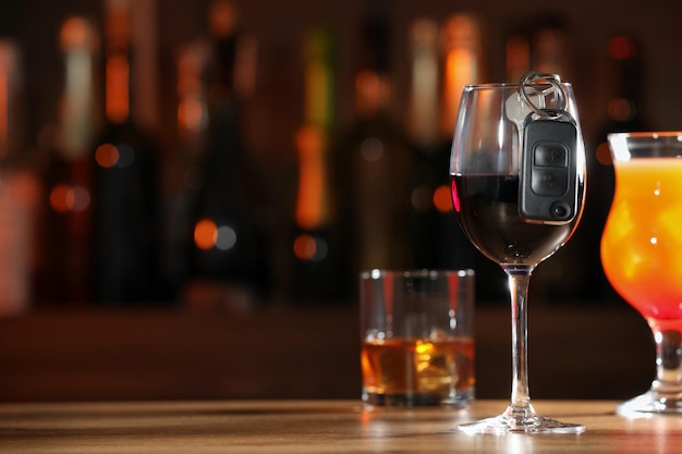 Car key and glass of alcoholic drink on table against blurred background space for text Drunk driving concept