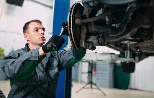 Car lifted in automobile service for fixing, worker repairs the wheel,