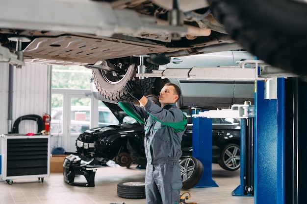 Car lifted in automobile service for fixing, worker repairs the wheel,