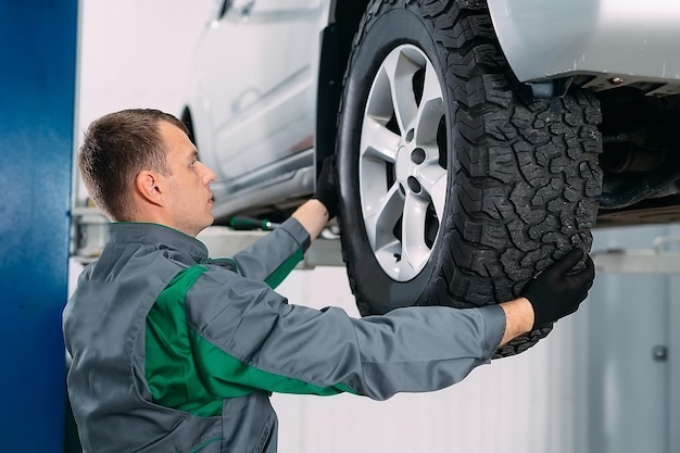 Car lifted in automobile service for fixing, worker repairs the wheel,