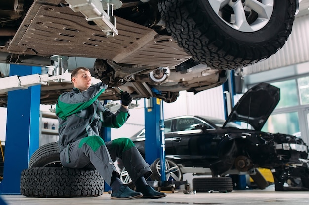 Car lifted in automobile service for fixing, worker repairs the wheel