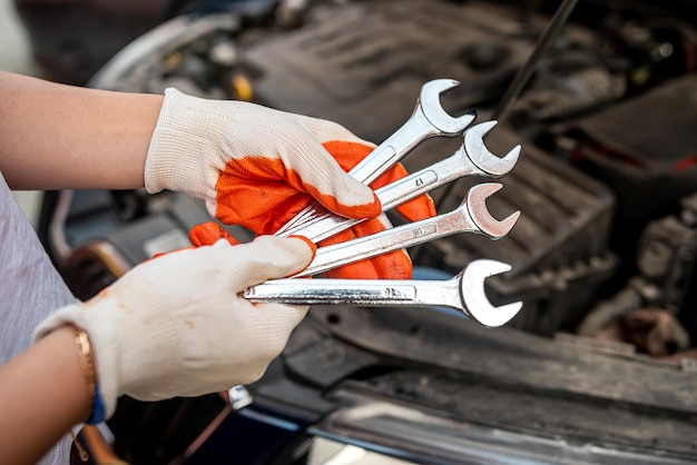 Car mechanic repairs a car engine near a car with an open hood