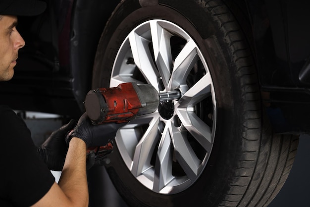 Car mechanic replacing car wheel of lifted automobile at repair service station assembly