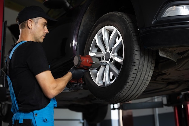 Car mechanic replacing car wheel of lifted automobile at repair service station assembly