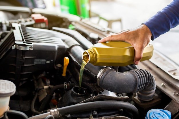 Car mechanic replacing and pouring fresh oil into engine at maintenance repair service station.