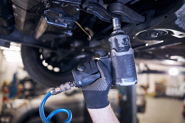 Car mechanic using impact wrench at auto repair station