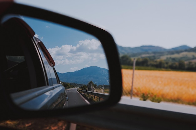 Car rear view mirror Road field and mountain reflection in mirror Traveling in Europe