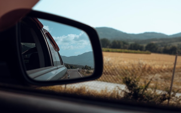 Car rear view mirror Road field and mountain reflection in mirror Traveling in Europe