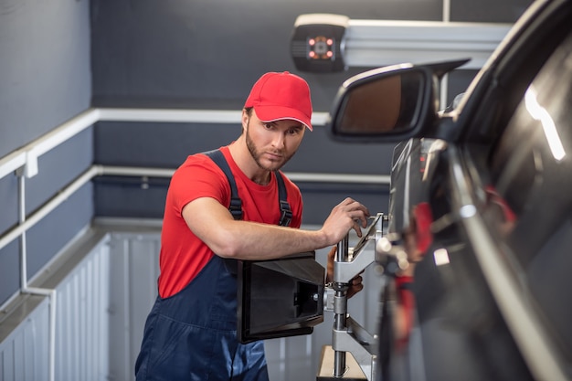 Car repair, wheel. Concentrated experienced young mechanic in work clothes checking car wheel in garage