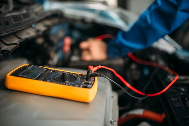 Car repairman with multimeter, battery inspection. Auto-service, vehicle wiring diagnostic, electrician occupation