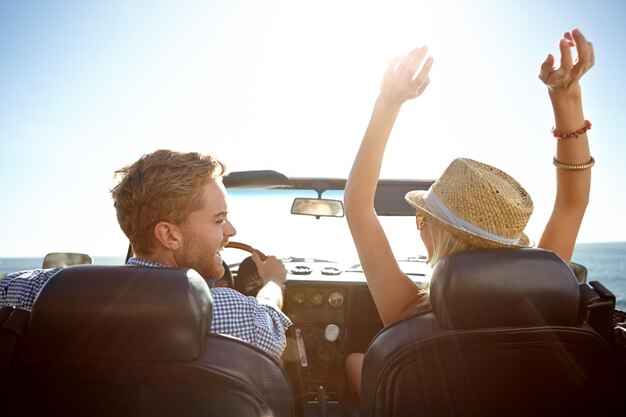 Car road trip and freedom with a couple by the beach on a drive to enjoy the view during summer together Travel transport and driver with a woman sitting hands raised by the ocean with her man