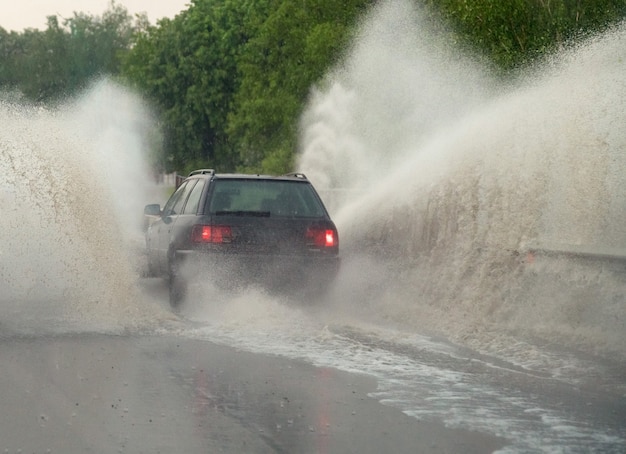 Car runs into big puddle at heavy rain, water splashing over the car. Car driving on asphalt road at thunder storm. Dangerous driving conditions