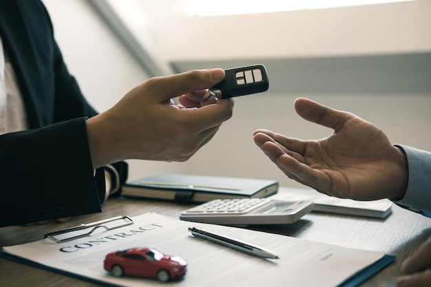 The car salesman is presenting the new car keys to the car buyer at the showroom after signing the contract