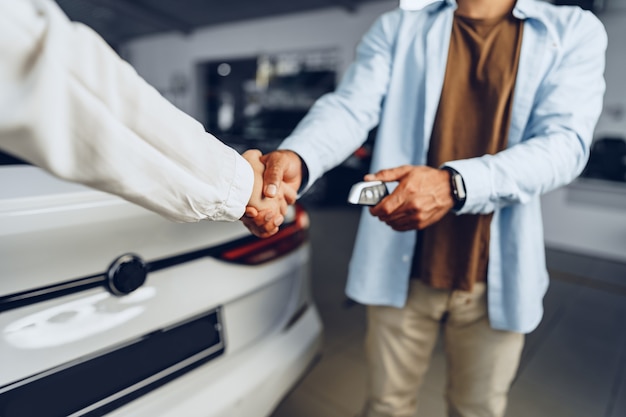 Car seller and buyer handshake at car dealership against a new car