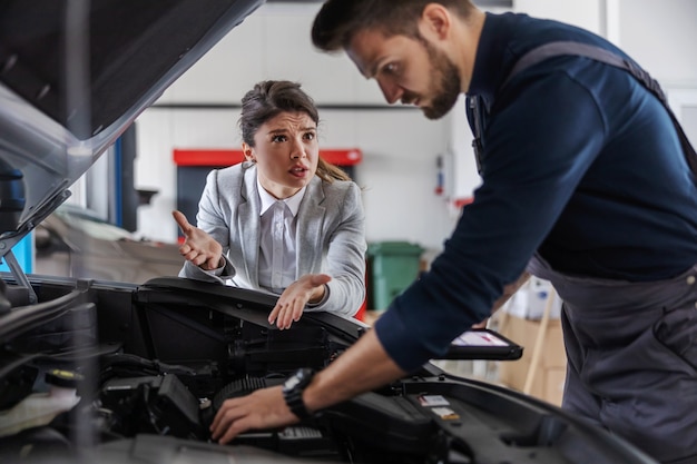 Car seller talking to a mechanic who is fixing car