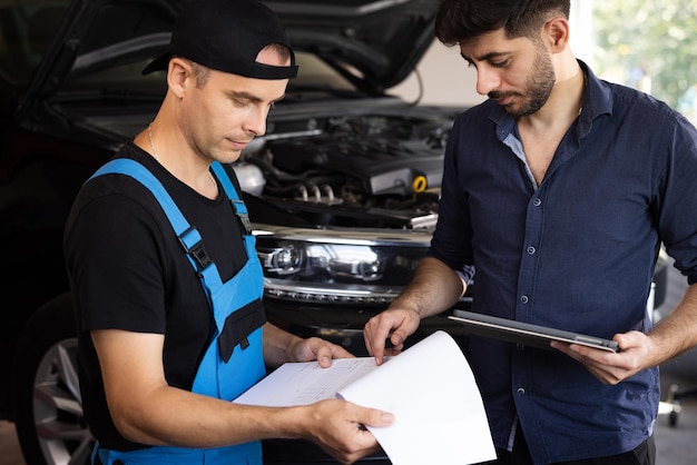 Car service employees inspect the bottom and skid plates of the car manager checks data on a tablet