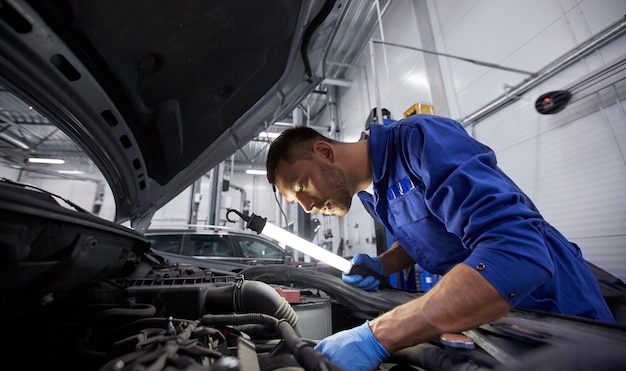 Photo car service, repair, maintenance and people concept - auto mechanic man with lamp working at workshop