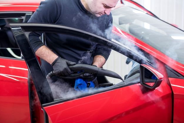 Car service worker cleans interiror with steam cleaner