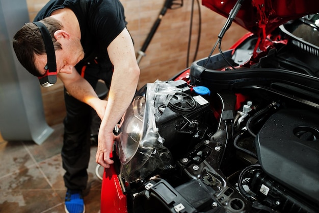 Car service worker put anti gravel film on a red car body at the detailing vehicle workshop. Car protection with special films.