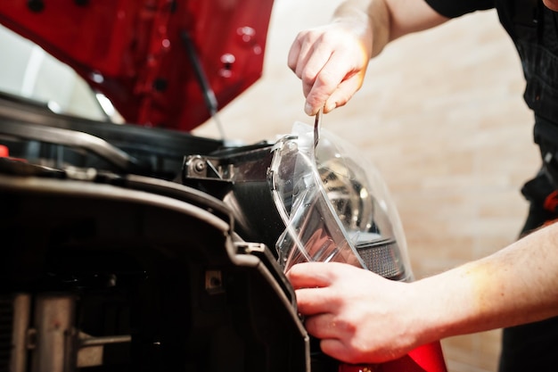 Car service worker put anti gravel film on a red car body at the detailing vehicle workshop Car protection with special films