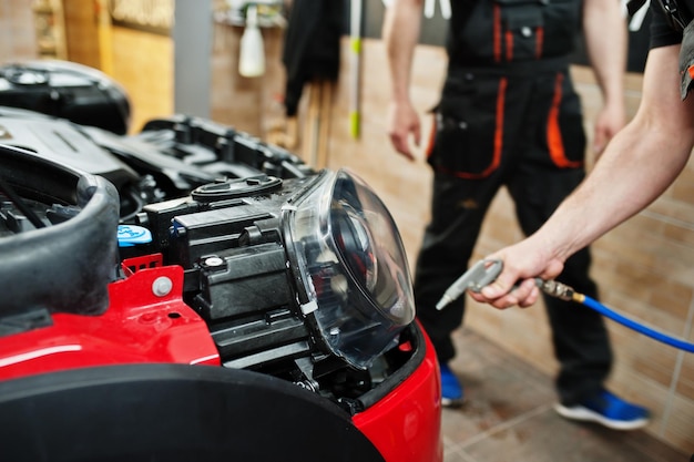 Car service worker put anti gravel film on a red car body at the detailing vehicle workshop Car protection with special films