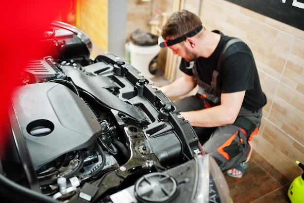 Car service worker put anti gravel film on a red car body at the detailing vehicle workshop Car protection with special films