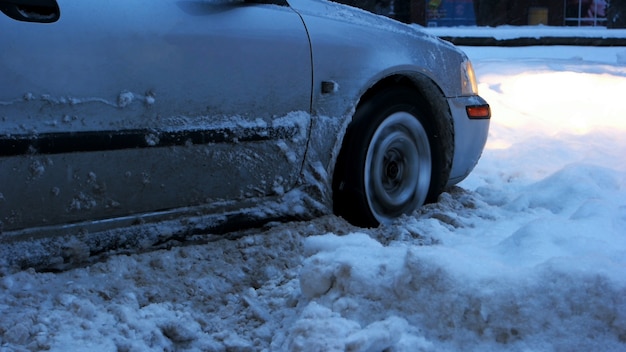 Car stalled in the snow. Close up of car wheel stuck in snow drift. Uncleaned streets with snowdrift after heavy snowstorm.