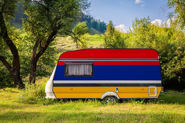 A car trailer, a motor home, painted in the national flag of Armenia stands parked in a mountainous. 