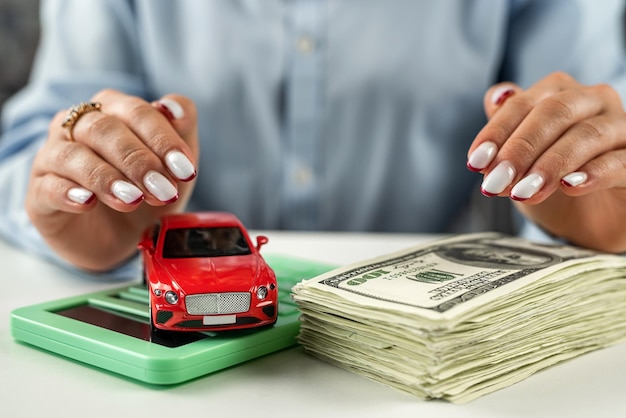 Car on US dollar bills and calculator on glass table with hands over car