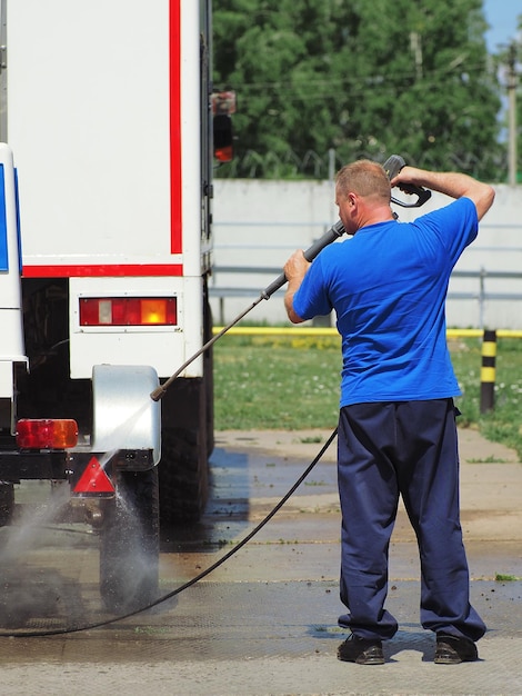 Car wash for heavy vehicles and trucks Male car wash worker washes a truck with a water gun on the street on a summer day