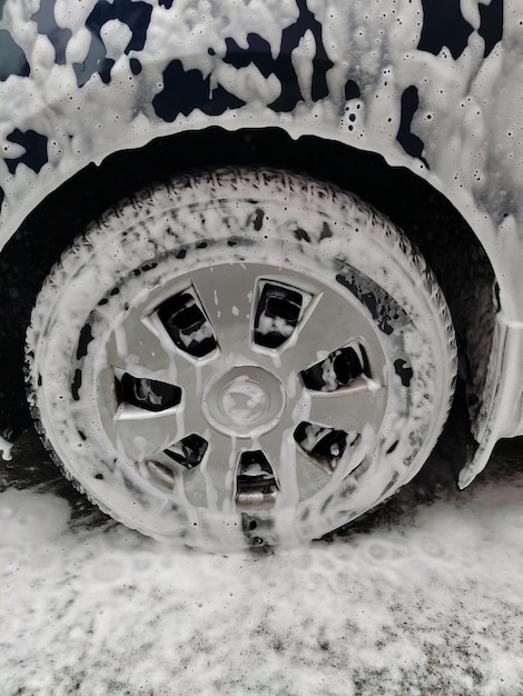 Car wheel in white washing foam with bubbles at car wash closeup