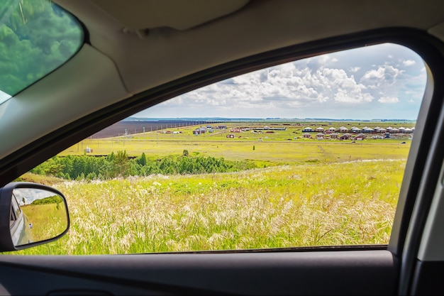 Car window with view of green meadow and clouds on the horizon on sunny summer day