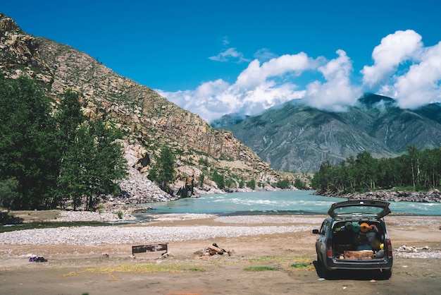 Car with open large trunk near mountain river with turquoise water. 