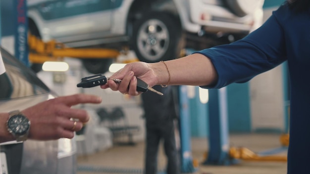 Car workshop - woman gives the keys of car for mechanic, telephoto