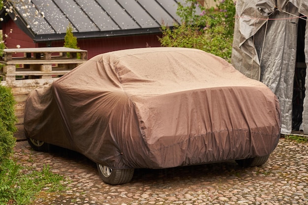 A car in the yard of a private house covered with a tarp