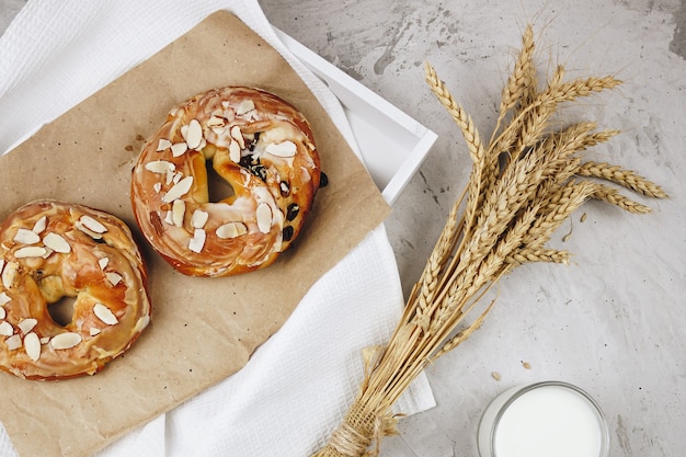 Caramel buns with raisins and almonds are lying on kraft paper in a tray. Next to it is a bouquet of wheat and rye ears, a mug with milk on a concrete background, selective focus.