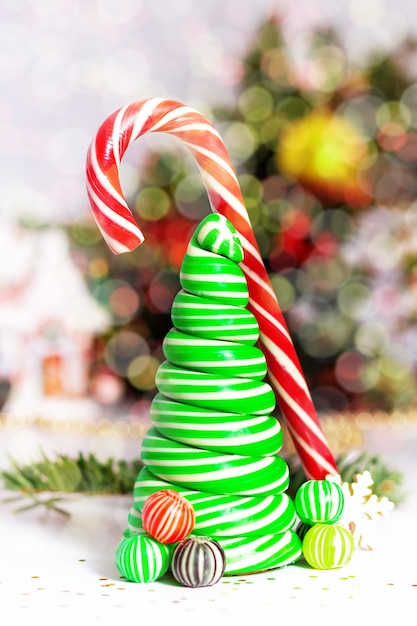 Caramel candy canes christmas tree with fun sweet balls christmas card concept striped christmas caramel tree  light up natural green fir tree with bokeh in background