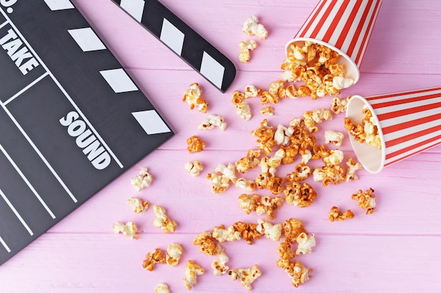 Caramel popcorn and movie clapper on color wooden background